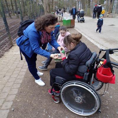 Rollstuhlfahrerin trinkt ein Trinkpäckchen, Betreuerin hilft beim festhalten 