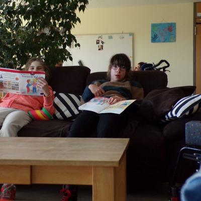 Zwei Schülerinnen sitzen auf dem braunen Sofa auf der Gruppe, die Wand ist gelbgestrichen, es liegen 2 gestreifte Kissen auf dem Sofa in schwarz-weiß gestreift. 