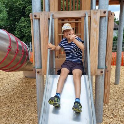 Ein Junge sitzt auf einer Rutsche und winkt.  