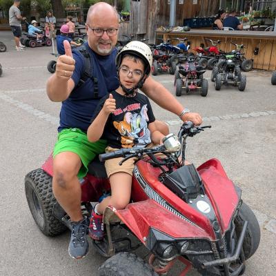 Ein Junge und ein Mann sitzen auf einem Quad und zeigen den Daumen nach oben.