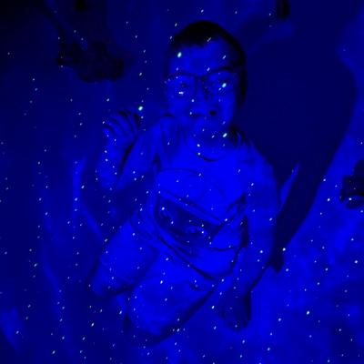 Ein Junge sitzt auf dem Boden. Der Raum ist erfüllt von einem blauen Sternenhimmel.