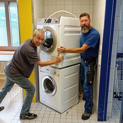Zwei Hausmeister verschieben eine Waschmaschinen Trockner Kombination