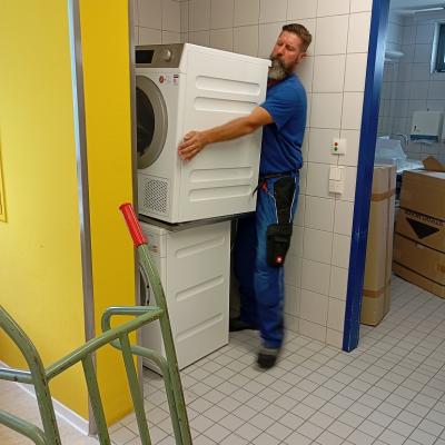 Ein Hausmeister hebt einen Trockner hoch