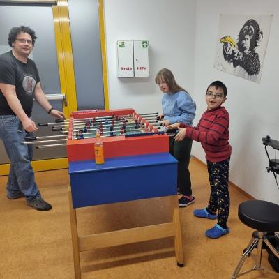 Zwei Schüler spielen mit einem Erwachsenen eine Runde Tischkicker.