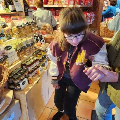 Schülerin steht mit ihrer lila, weisen Jacke im Brezel Huber Laden, schaut interessiert was es gibt und was sie kaufen kann