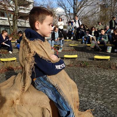 Ein Junge sitzt in einen Sack gehüllt auf einem Hocker.