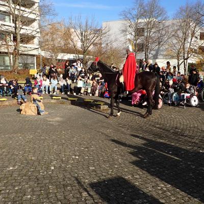 Kinder, Jugendliche und Erwachsene im Rondell, zum Teil im Rollstuhl, manche mit Laternen. Sankt Martin kommt mit seinem Pferd zum Bettler.