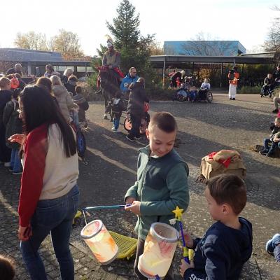 Kinder mit Laternen im Vordergrund, im Hintergrund Sankt Martin auf em Pferd, Kinder stehen zum Füttern an