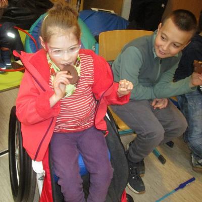 Ein Mädchen im Rollstuhl beißt in einen Lebkuchen, rechts daneben ein Junge, ebenfall mit Lebkuchen in der Hand