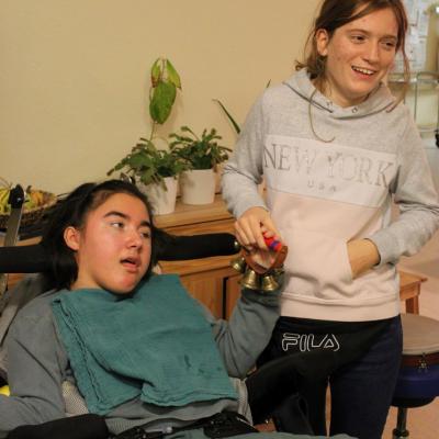 zwei junge Frauen halten gemeinsam ein Schelleband, eine davon sitzt im Rollstuhl