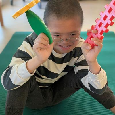 Ein Junge sitzt auf dem Boden mit Spielzeug in der hand und schaut in die Kamera