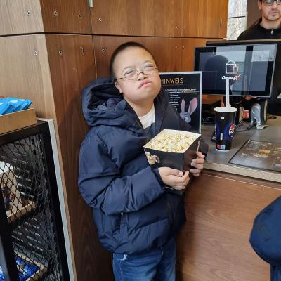 Ein Junge steht vor dem Tresen und hält eine Tüte Popcorn vor sich. 