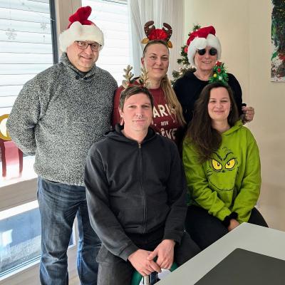 2 Männer, 3 Frauen haben weinachtlichen Haarschmuck auf dem Kopf und lachen in die Kamera