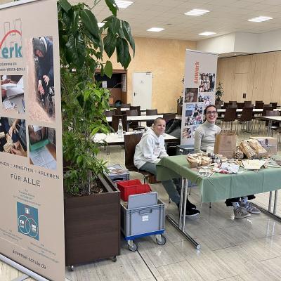 Die Schüler sitzen am Verkaufsstand, und warten auf die Käufer. Im Hintergrund sind Esstische zu sehen