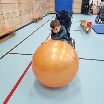 Ein Junge im Rollstuhl spielt mir einem großen Orangenen Pezziball 