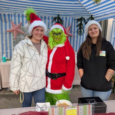 Der Grinch und zwei Frauen lachen beim Weihnachtsmarkt der AHWerner Schule in die Kamera