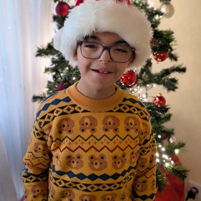 Ein Junge schaut lachend in die Kamera und hat eine Weihnachtsmütze auf