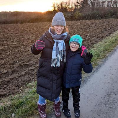 Ein Junge und ein Mädchen stehen Arm in Arm am Feldrand bei Sonnenuntergang und schauen in die Kamera
