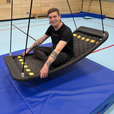 Ein Mann sitzt in der Netzschaukel und lacht in die Kamera