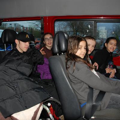 Maik, Marija, Sophia, Luca und Ghofran sitzen auf den Rückbänken des Schulbusses. Manche lächeln in die Kamera. Links liegen viele Jacken auf einem Haufen.