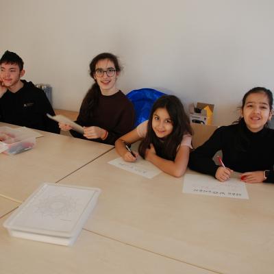 An einem Tisch sitzen Maik, Marija Sophia und Ghofran. Sie schreiben ihre Namen auf ihre Zimmerschilder.