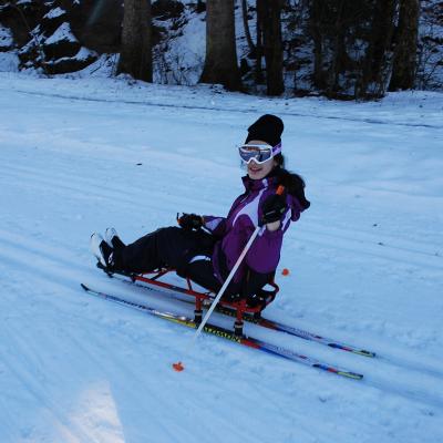 Marija fährt im Skischlitten in der Loipe und lächelt dreht sich zur Kamera. Sie lächelt.