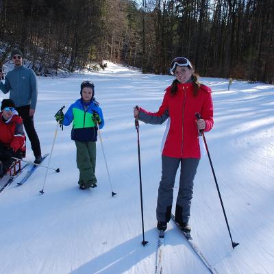 Maik, Herr Kling, Luca und Lena sind im Schnee und lächeln in die Kamera. Im Hintergrund sieht man Bäume und deren Schatten.