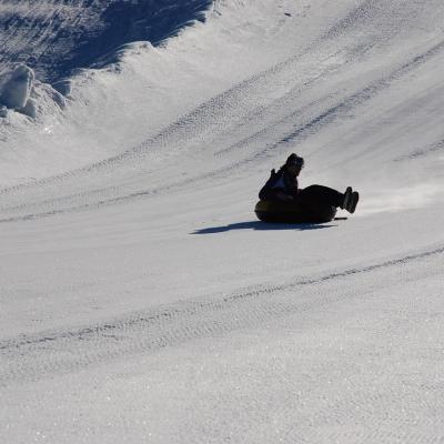 Vor dem Schneehang fährt Marija denselben in ihrem Reifen herunter. Man sieht sie im Gegenlicht als dunkle Silhouette.