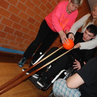 Marik rollt eine Kugel über zwei parallele Billard-Queues. Er wird von Frau Gauch unterstützt, sowie von Frau Rothmund und Herrn Lazergui von den Stuttgartern.