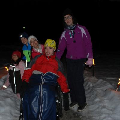 Sophia, Luca, Ghofran, Maik und Marija stehen auf einem Weg, der rechts und links von brennenden Fackeln gesäumt ist, die im Schnee stecken.