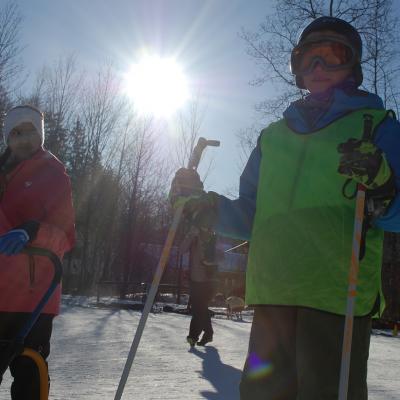 Ghofran schaut herausfordernd herüber zu Luca. Beide stehen an der Startlinie der Rennstrecke. Dahinter strahlt die Sonne über ein paar Bäumen.