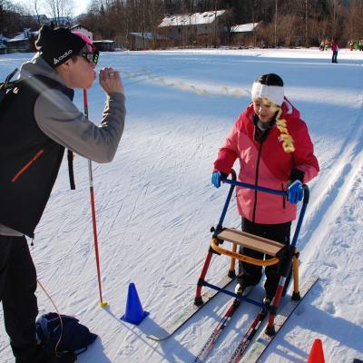 Ghofran läuft am Skilator ins Ziel ein, das durch zwei Pylonen markiert ist. Frau Gauch empfängt sie, indem sie eine Luftschlange bläst, die sich entrollt.