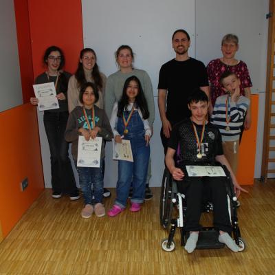 Marija, Lena, Frau Fecke, Herr Kling, Frau Gauch, Sophia, Ghofran, Maik und Luca lächeln in die Kamera. Die Kinder halten ihre Urkunden und Medaillen.