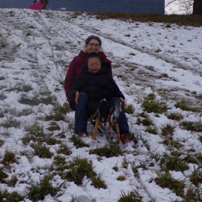 Ein Junge und eine Frau sitzen zusammen auf einem Holzschlitten. Sie fahren den Berg herunter 