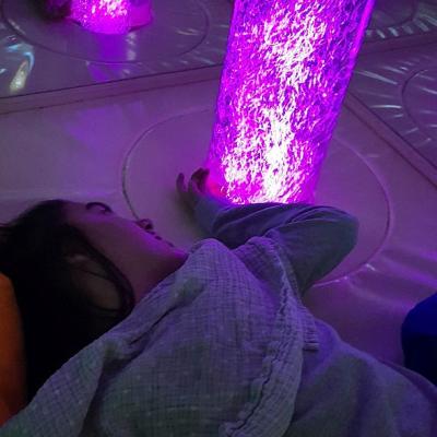 Eine junge Frau liegt an einer beleuchteten Wassersäule. Es leuchtet lila.