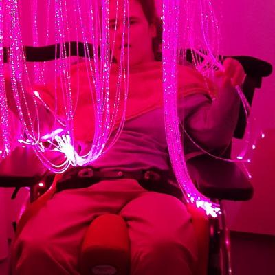 Eine junge Frau im Rollstuhl steht in einem Lichtervorhang. Er leuchtet rot.