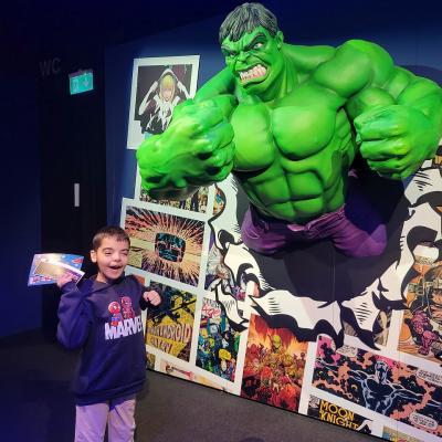 Ein Junge steht vor der Hulk Figur und lacht in die Kamera