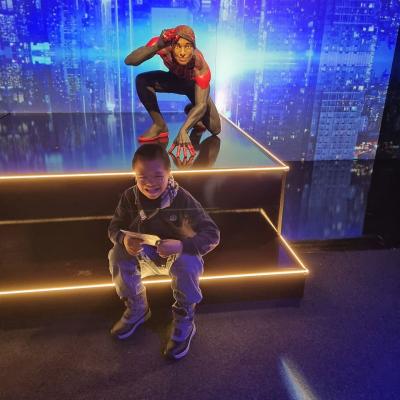 Ein Junge sitzt auf einer schwarzen beleuchteten Treppe. Hinter ihm auf einem Podest ist eine Spiderman Figur. 