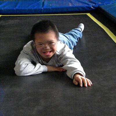 Ein Junge liegt auf dem Bauch auf einem Trampolin. Er lacht in die Kamera