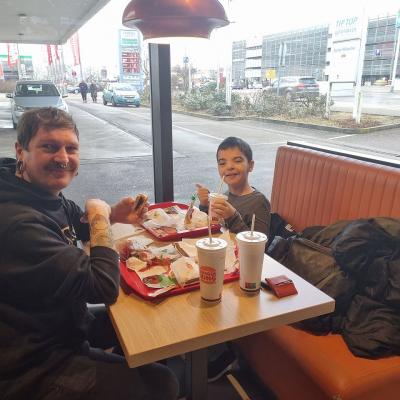 Ein Mann und ein Junge sitzen an einem Tisch in einem Fast-Food Restaurant und essen Burger 