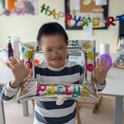 Ein Junge schaut lachend durch einen Luftballon in die Kamera. 