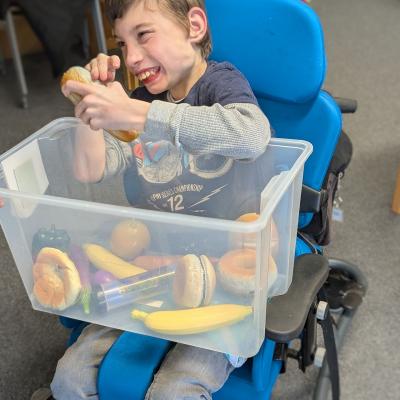 Ein Junge im Rollstuhl spiel mit einer Kiste voller Rasseln und lacht