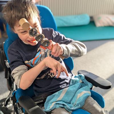 Ein Junge im Rollstuhl hat ein Klangspiel/Rassel in der Hand und freut sich