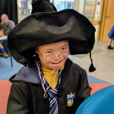 Ein Junge im Zauberer Kostüm lacht. Er hat einen Spitzen Hut auf. 