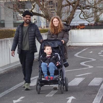 Ein Mann, ein Mädchen und ein Junge im Rollstuhl laufen lachend zusammen über den Platz.