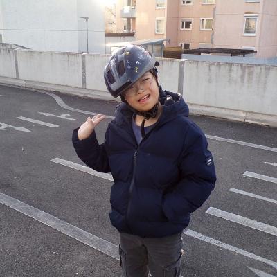 Ein Junge lacht in die kamera, winkt und hat einen Fahrradhelm auf. 