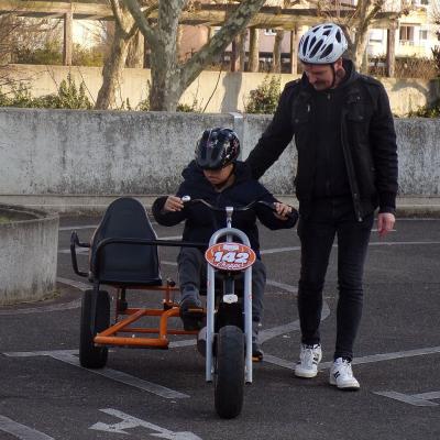 Ein Junge übt Kettcar fahren und ein Mann begleitet ihn dabei. Beide haben Fahrradhelme an. 