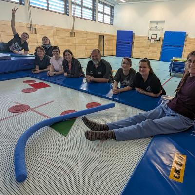 9 Personen sind am Trampolin versammelt und lachen in die Kamera