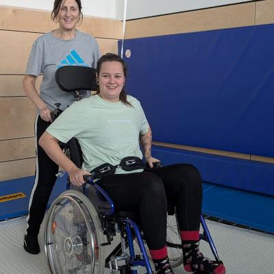 Eine Frau im Rollstuhl und eine Frau zur Unterstützung springen auf dem Trampolin, beide lachen