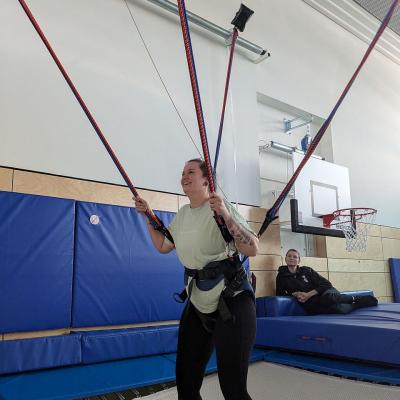 Eine Frau ist an Sicherungsseilen gesichert auf dem Trampolin, damit sie sehr hoch springen kann